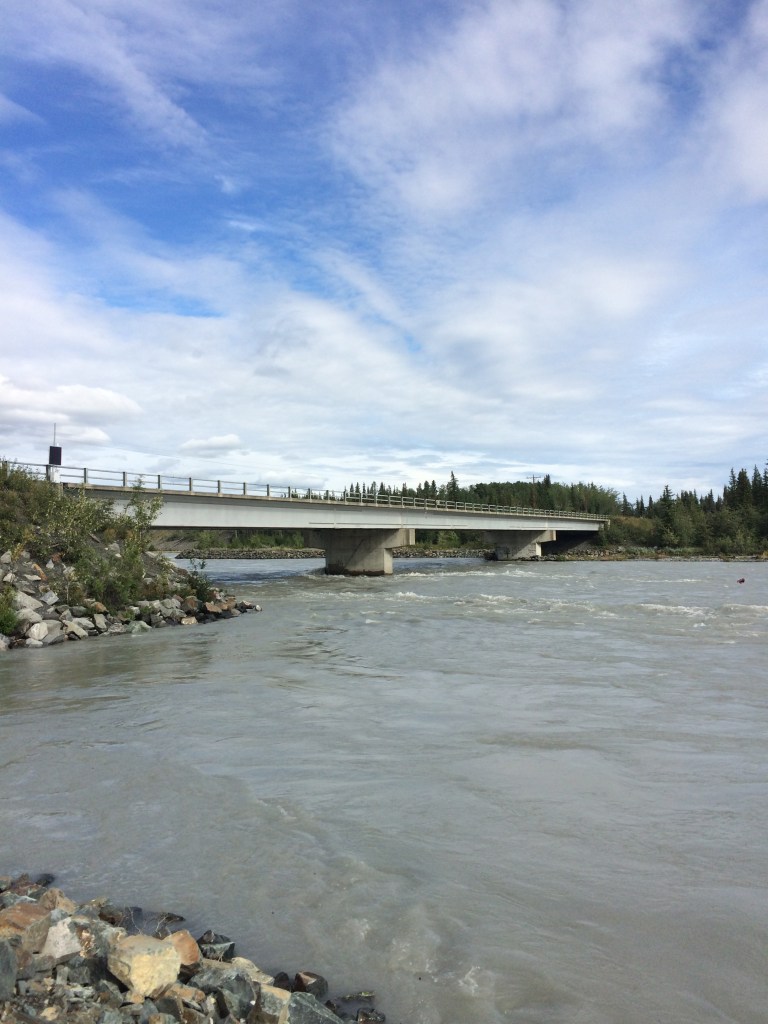 A full Tazlina river below a concrete and steel girder bridge.