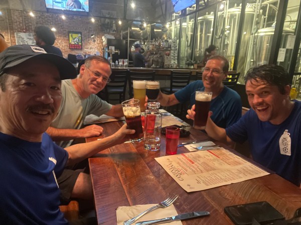 4 runners around a table inside Human Robot offering toasts with glasses full of beer