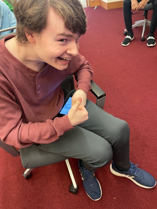 Seated student with injured knee and forced grin giving thumbs up